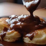 A close-up of freshly made chocolate gravy recipe poured over warm biscuits